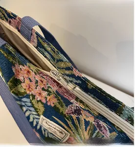 Detail of silver metal zipper and woven handle on blue floral jacquard tote bag