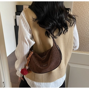 Détail du sac croissant en daim marron gaufré léopard avec pompon rouge décoratif