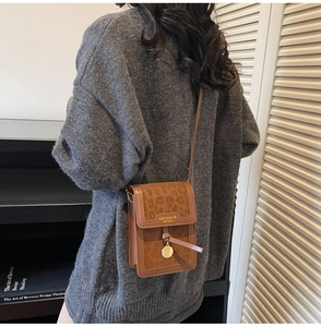 Close-up of brown faux leather crossbody bag with leopard print flap and gold pendant