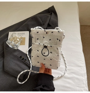 Detailed view of white quilted mini phone bag with black bow patterns and braided strap