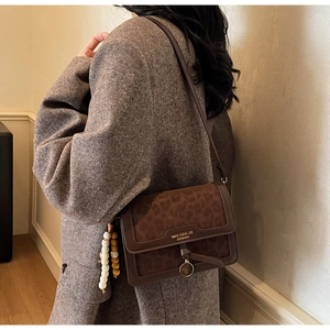 Détail du sac bandoulière léopard avec pendentif perles et logo de marque sur le rabat
