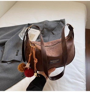 Gros plan du sac bourse en daim marron avec un porte-clés décoratif en boules de peluche
