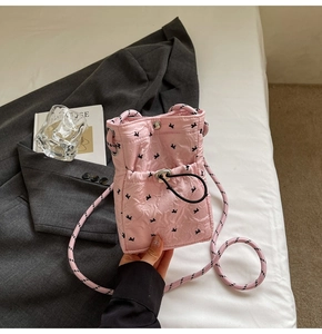 Detail of pink quilted mini crossbody bag with black bow embroidery and rope strap