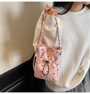 Pink quilted crossbody phone bag with bow patterns and woven rope strap shown on model