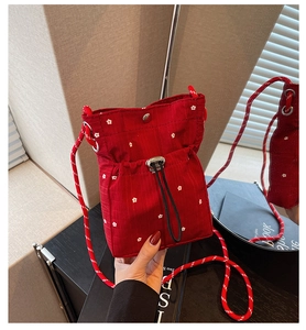 Detail of red fabric pleated crossbody bag with small white floral patterns and drawstring