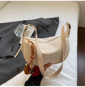 Détail du sac dumpling en cuir crème avec bandoulière large et breloques en fourrure