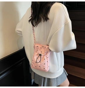 Pink quilted nylon crossbody bag with drawstring closure and bow detail shown on model