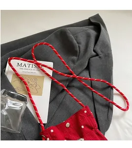 Detailed view of red floral fabric crossbody bag with woven rope strap and metal snap