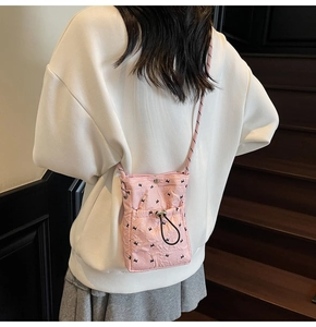 Detail of light pink quilted phone bag showing drawstring pocket and woven strap on model