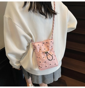 Detail view of pink pleated phone bag with bow embroidery and woven strap worn by model
