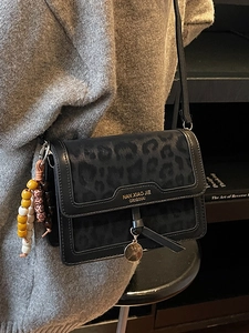 Sac bandoulière noir chic avec gaufrage léopard porté par un mannequin dans une bibliothèque