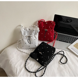 Close-up of pleated drawstring crossbody bags in black, white and red with floral embroidery