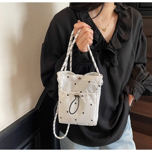 Detailed shot of white pleated crossbody bag with floral embroidery and woven strap