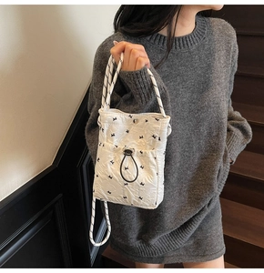 Detail of white quilted crossbody bag with black bow patterns and rope handles