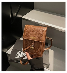 Detail of dark brown faux crocodile leather bag with gold logo and round pendant
