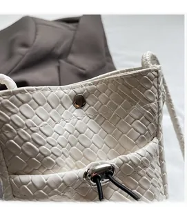 Detail of white woven leather crossbody bag featuring metal snap button and drawstring closure