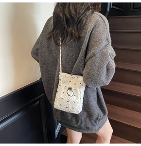 Detail of white quilted crossbody bag featuring small black bows and drawstring closure