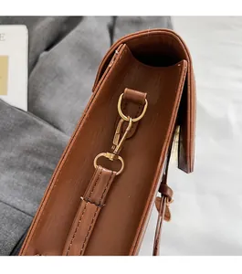 Detailed close-up of brown textured leather bag with premium gold metal hook clasp