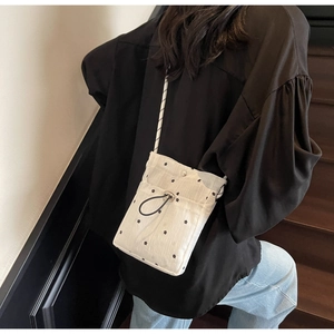 Detail of a white floral crossbody bag with black drawstrings and a braided strap