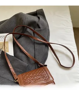 Close-up of brown woven crossbody bag with adjustable strap and metallic logo detail