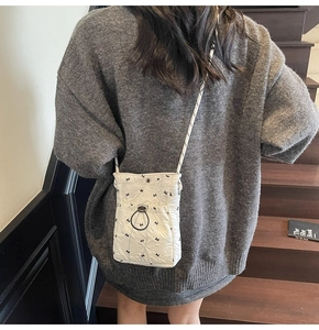 Detail of white quilted crossbody phone bag featuring black bows and drawstring closure