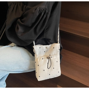 Close-up of white mini crossbody bag with black star print and drawstring pocket detail