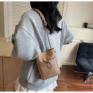 Detailed back view of a khaki woven crossbody phone bag worn by a model in a modern home