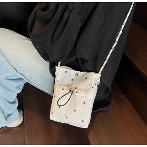 Detail of white floral crossbody bag with black drawstring pocket on a wooden background