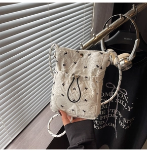 Detail of white quilted crossbody phone bag featuring black bow prints and woven strap