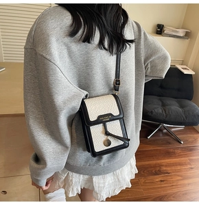 Detail of mini black and white crossbody bag with crocodile texture and gold tassel charm