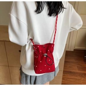 Detail of red floral drawstring crossbody bag worn over white sweater with rope strap