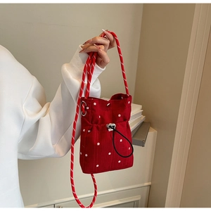 Detail of red floral bucket bag featuring white flower patterns and woven rope strap