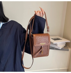 Detail of a brown woven leather crossbody phone bag with gold logo and adjustable strap