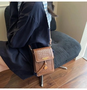 Detail of a brown woven leather crossbody phone bag with gold metal pendant and shoulder strap