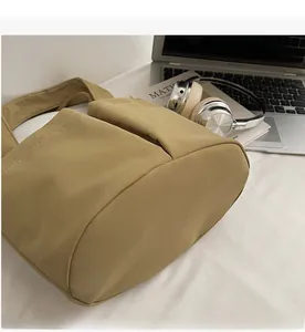 Dettaglio del morbido tessuto kaki di una borsa a secchiello capiente con laptop e libro