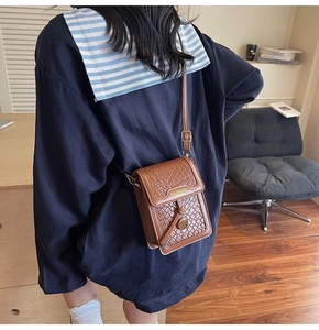Detail of brown woven crossbody bag with brand logo and gold strap adjustment buckle