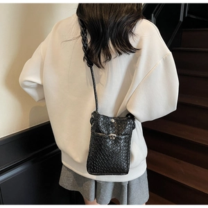 Detail of black woven mini crossbody bag with metal twist lock on white hoodie