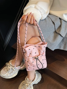 Pink quilted crossbody bag with black drawstrings and patterned strap lifestyle view