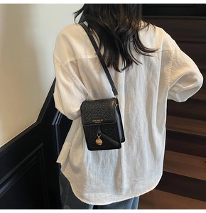 Detail view of black crossbody phone bag with woven texture flap and golden brand logo