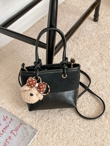 Vintage black bucket bag with plush bear charm on soft rug, crossbody and handbag style