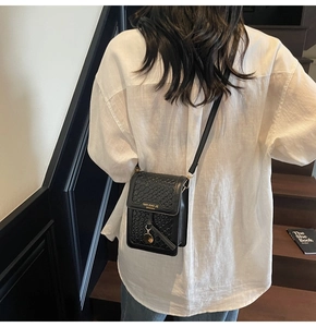 Detail of black mini crossbody bag featuring crocodile texture and gold circular pendant