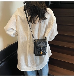 Detail of black woven texture crossbody bag with gold logo on a white shirt background