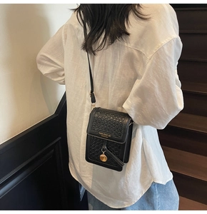Detail of black woven crossbody bag with gold lettering shown on a model