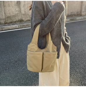 Dettaglio della borsa tote in tela kaki chiaro con due grandi tasche frontali e tracolle larghe