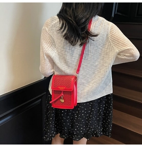 Detail view of a red woven crossbody phone bag with gold pendant on a model in-situ