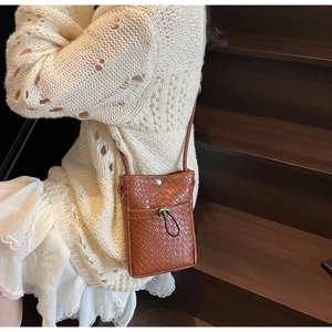 Close-up of brown textured crossbody bag with drawstring pocket on wooden stairs