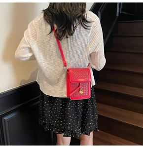 Detail of red woven crossbody bag with gold charm on a model in a minimalist setting
