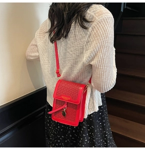 Detail of red woven leather phone bag with gold metal logo and adjustable strap worn by model