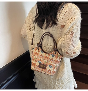 Detailed shot of geometric patchwork bucket bag worn over white crochet sweater