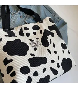 Detail shot of corduroy tote bag featuring a cow print pattern and branded fabric label